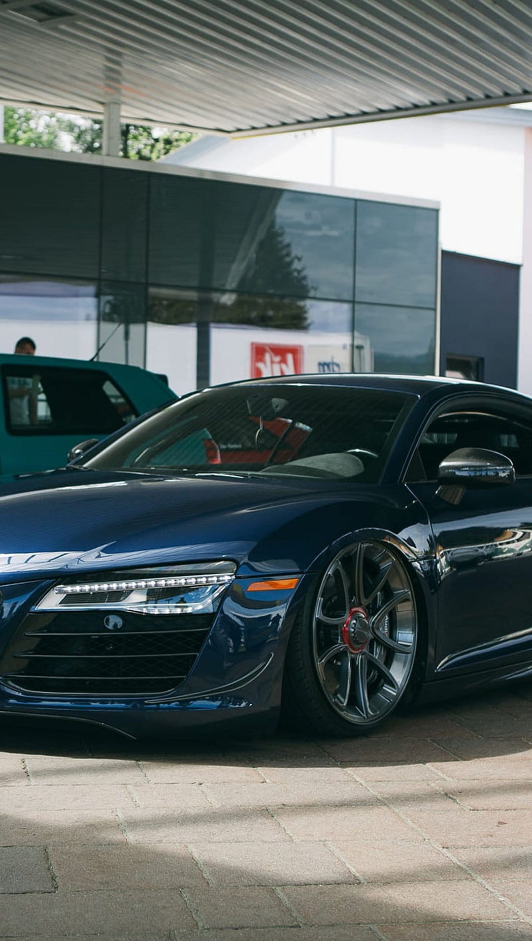 Blue Audi R8 sports car with red-accented black wheels parked at a modern gas station under bright canopy lights.