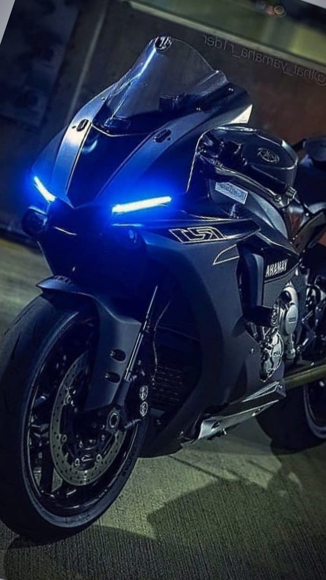 Yamaha R1 sportbike front fairing with glowing blue LED lights and visible disc brakes in a dark setting.