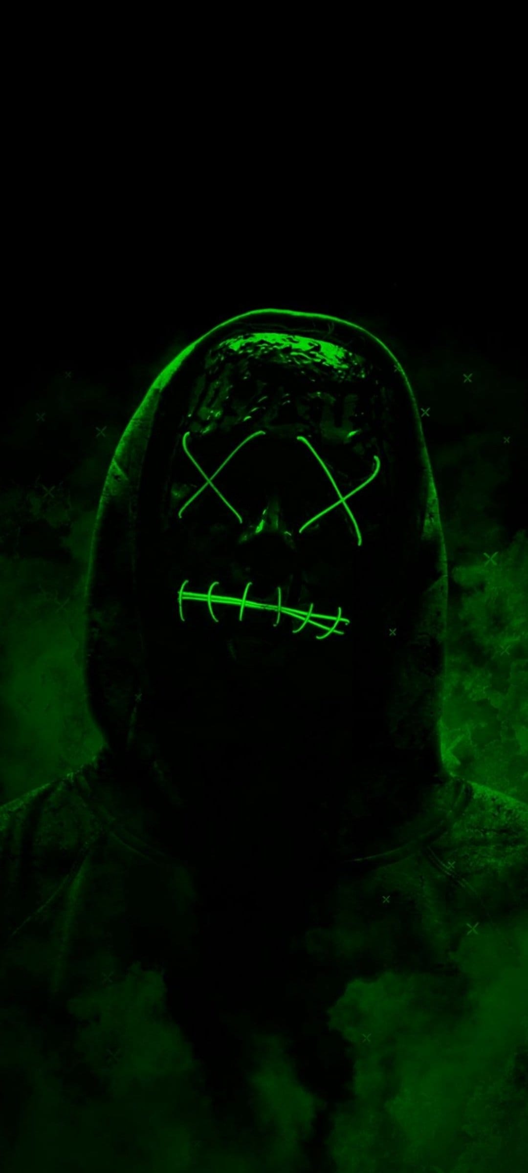 Person in a black hoodie wearing a glowing neon green mask with X-shaped eyes against a dark smoky background.