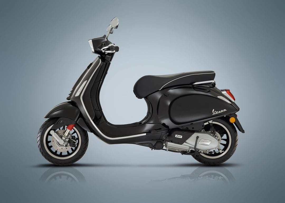 Matte black Vespa scooter side profile with silver accents and red suspension on a blue-grey background.
