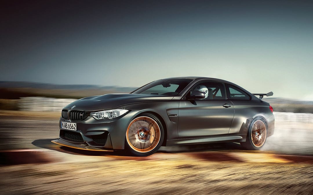 Matte grey BMW M4 GTS drifting on a sunlit track with smoking tires and blurred orange wheels in landscape view.
