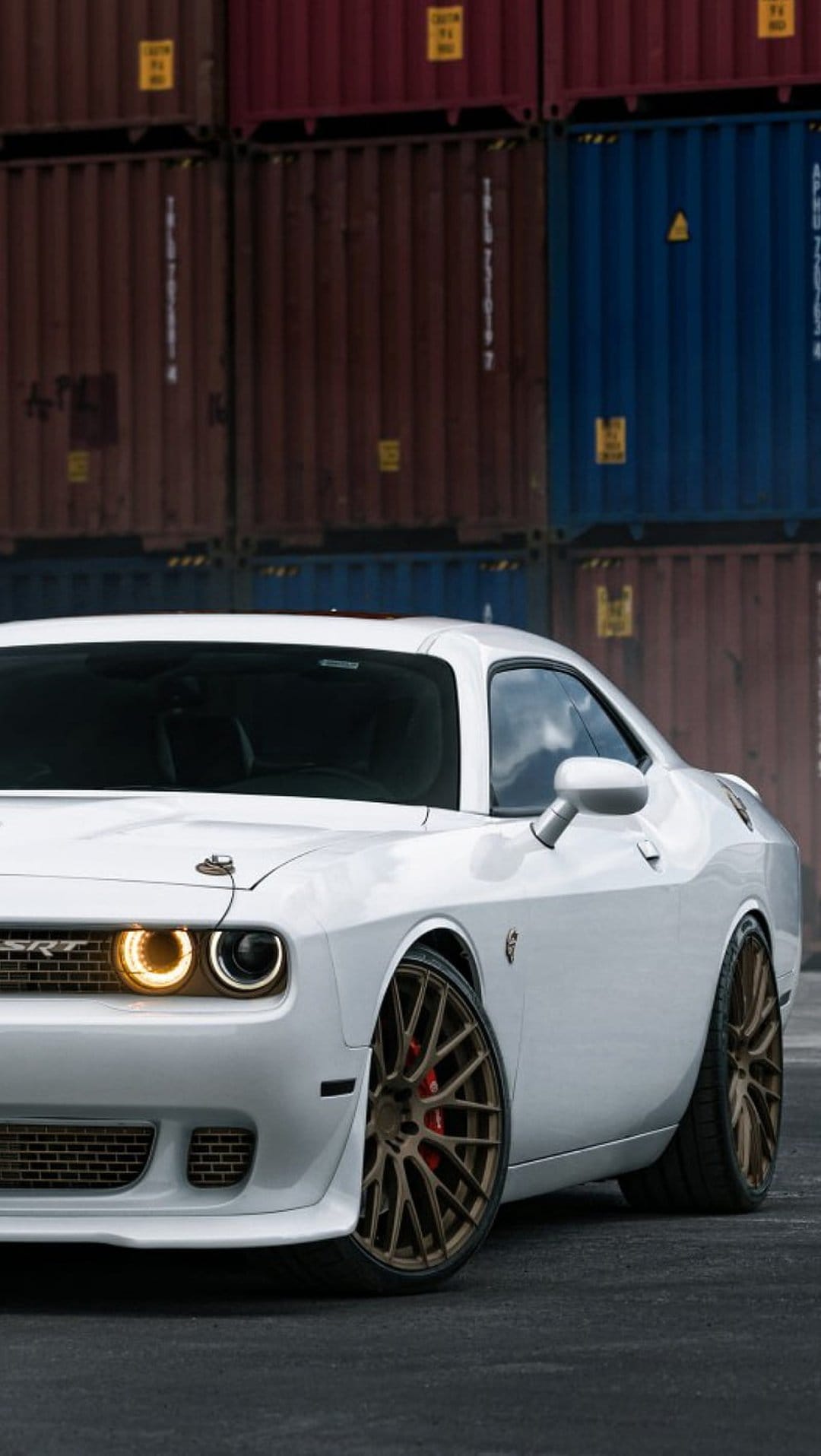 White Dodge Challenger SRT with bronze wheels and yellow headlights parked near industrial shipping containers