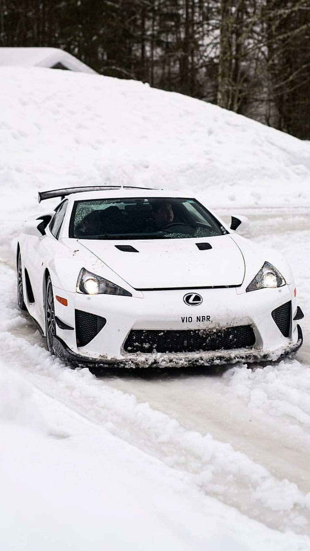 White Lexus LFA supercar maneuvers through a snow-covered road surrounded by frozen trees and soft winter light.