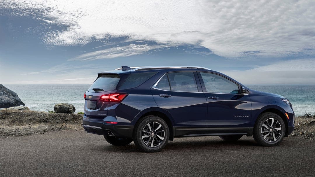Dark blue SUV parked on a coastal road overlooking the ocean under a cloudy sky with rocky cliffs.