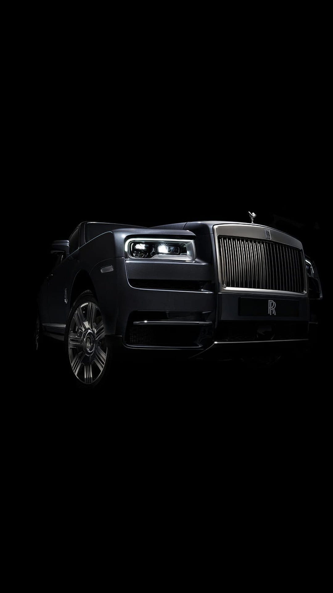 Rolls-Royce Cullinan SUV front grille and Spirit of Ecstasy ornament illuminated against a dark black background.