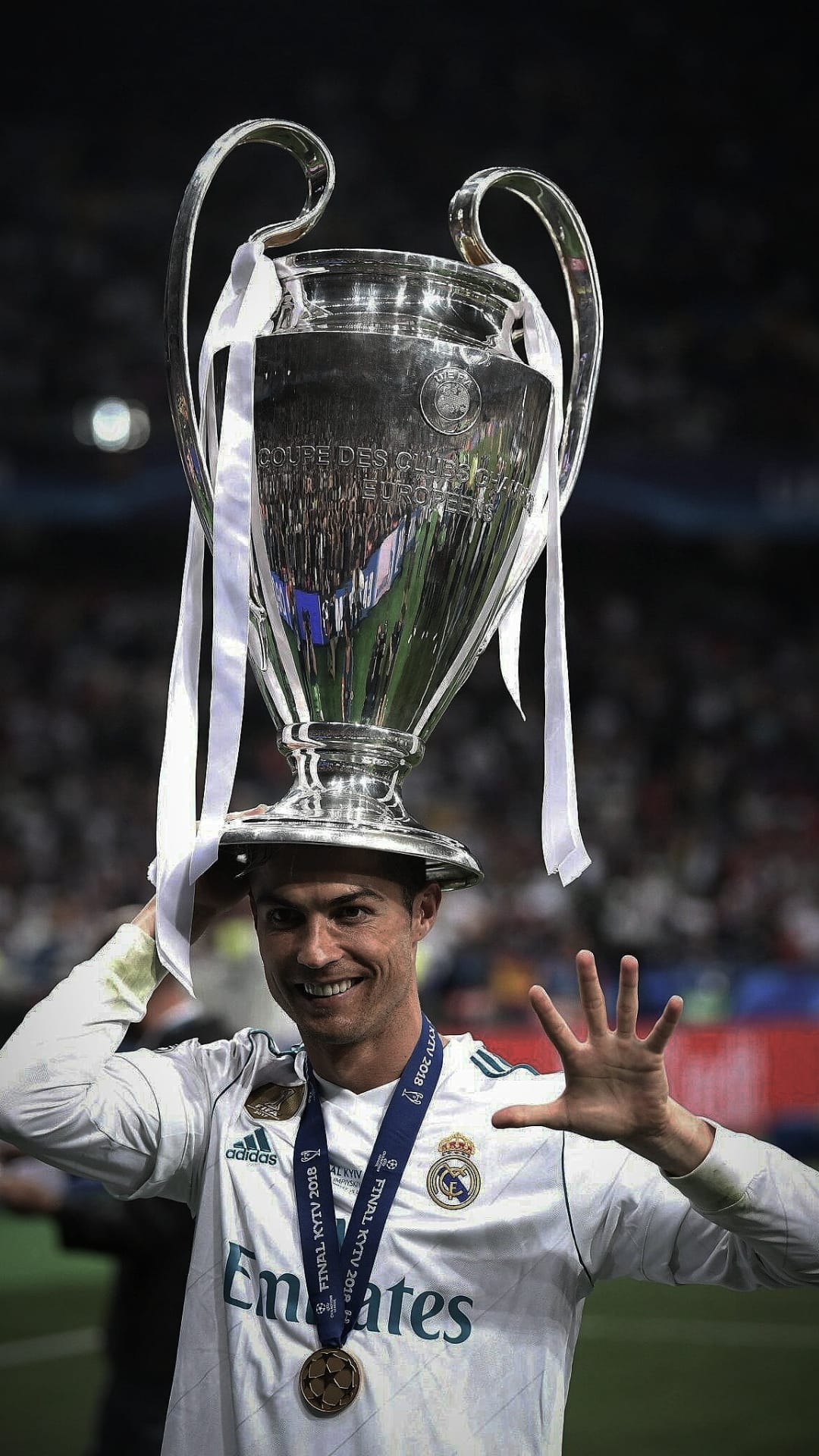 Cristiano Ronaldo holds the silver Champions League trophy while wearing a white Real Madrid football kit.
