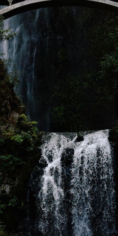 Waterfall, nature, bridge, powerful, cascading water, green foliage, serene, natural beauty, outdoors, landscape, wet, misty, vibrant, travel, destination, water flow, majestic, arch, mossy rocks, fresh.