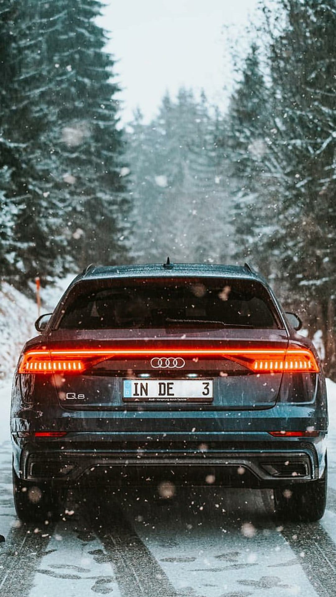 Audi Q8 SUV rear view with red taillights on a snow-covered forest road during a heavy winter snowfall.