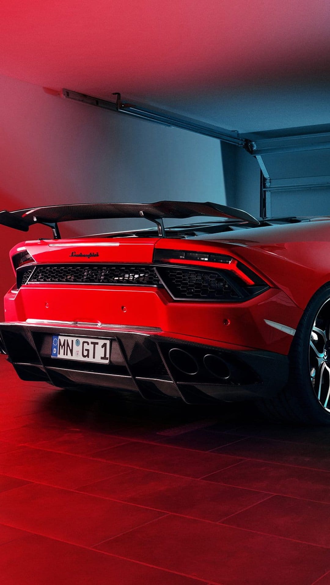 Red Lamborghini Huracan GT rear view with a large spoiler and glowing taillights under blue and red garage lights.