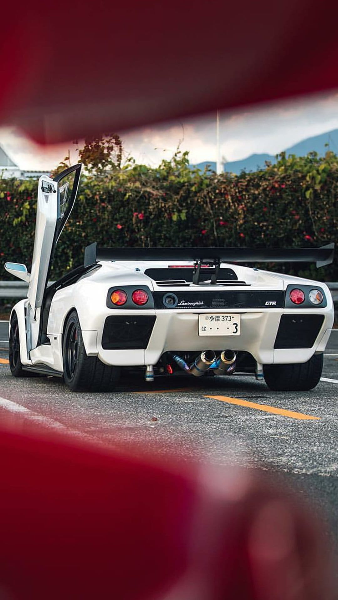 White Lamborghini Diablo GTR with open scissor doors and a large rear spoiler parked on a scenic mountain road.
