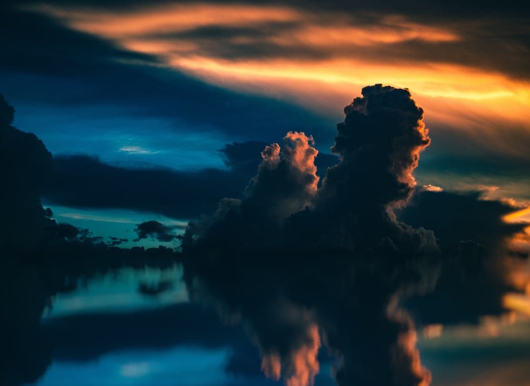Vibrant orange storm clouds mirror in a still lake at dusk, creating a symmetrical natural landscape scene.