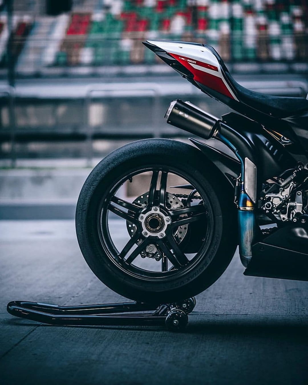 Sportbike rear wheel with a red and white tail section, disc brake, and exhaust pipe on a textured asphalt track.