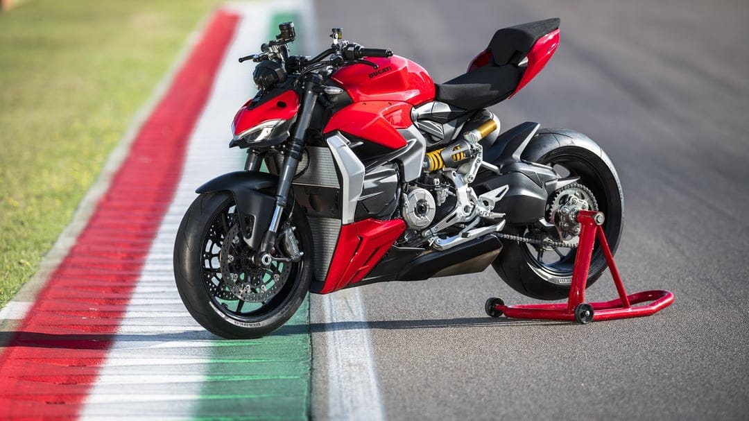 Red Ducati Streetfighter motorcycle on a paddock stand at a racetrack with green, white, and red curbing.