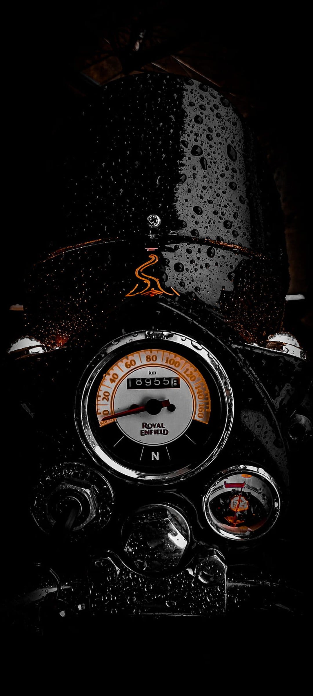 Royal Enfield speedometer covered in water droplets with a visible odometer and logo in dark, moody lighting.