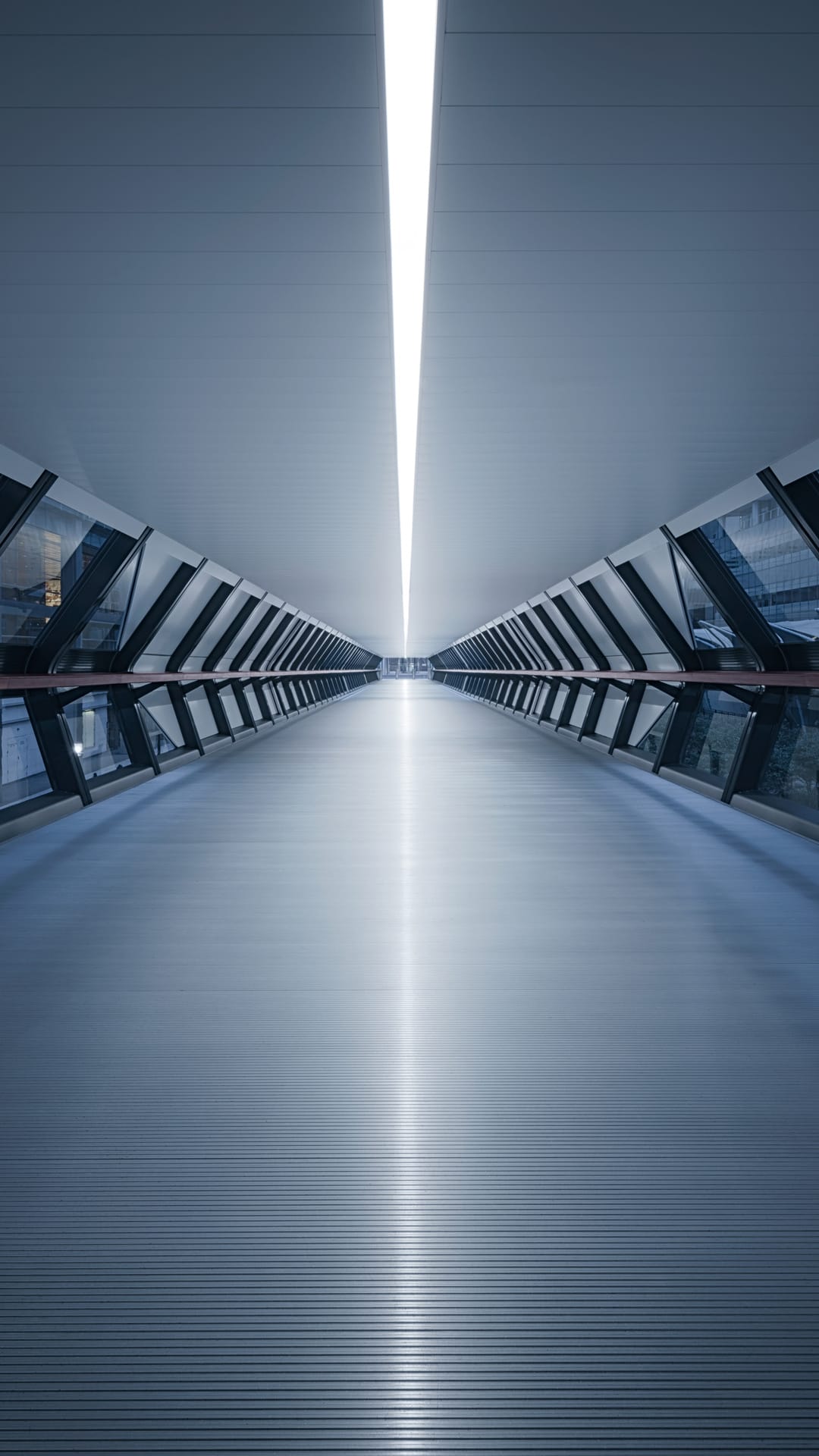 Blue symmetrical tunnel with a bright central light strip leading to a distant vanishing point inside a bridge.