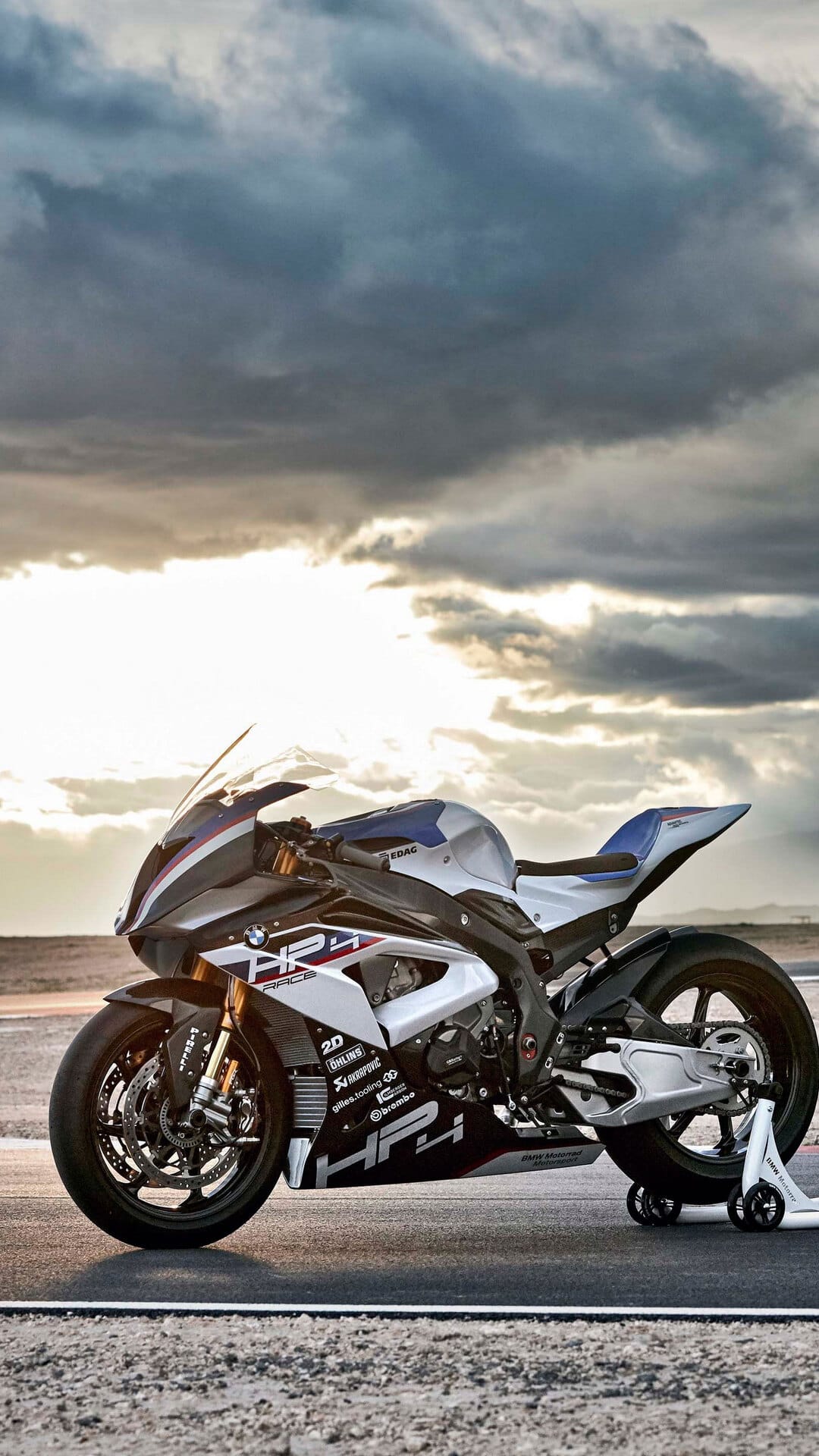 BMW HP4 Competition superbike on a racetrack under a cloudy sky with a sandy desert landscape in the background.
