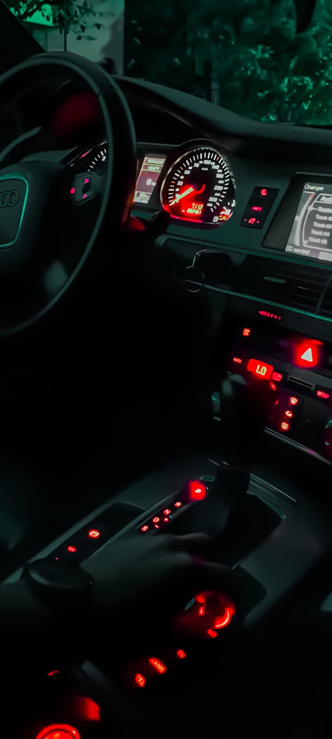 Red illuminated Audi dashboard features a glowing speedometer and center console buttons in a dark cabin.