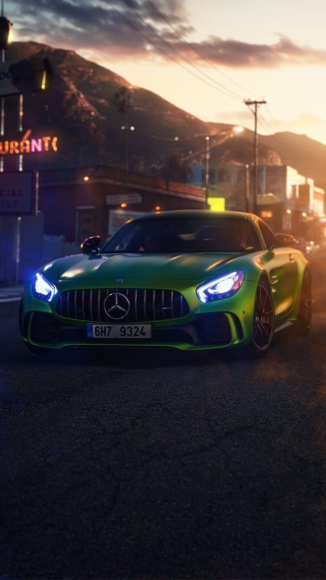 Green Mercedes-AMG GT parked on a city street with neon signs and sunset orange light reflecting on its surface.