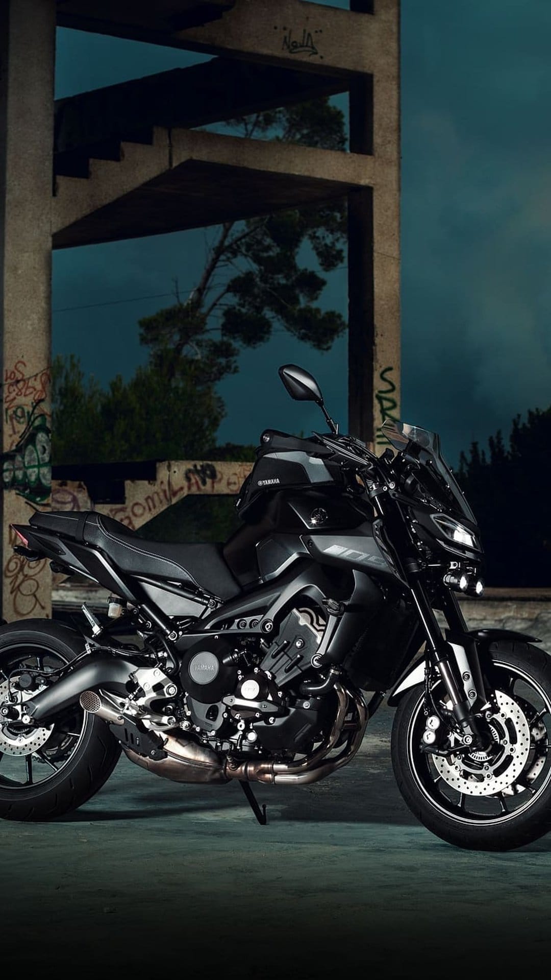 Black Yamaha MT-09 motorcycle parked near a graffiti-covered concrete pillar in a dark abandoned building.