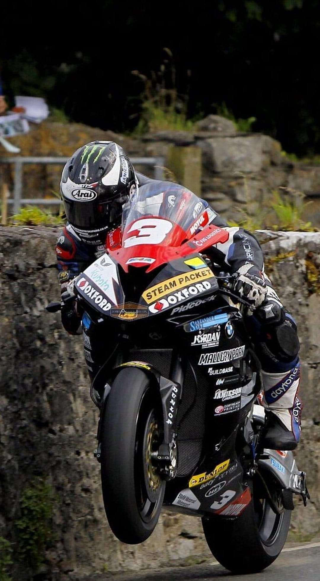 Professional racer executes a vertical wheelie on a red and black sportbike during a high-speed track competition.