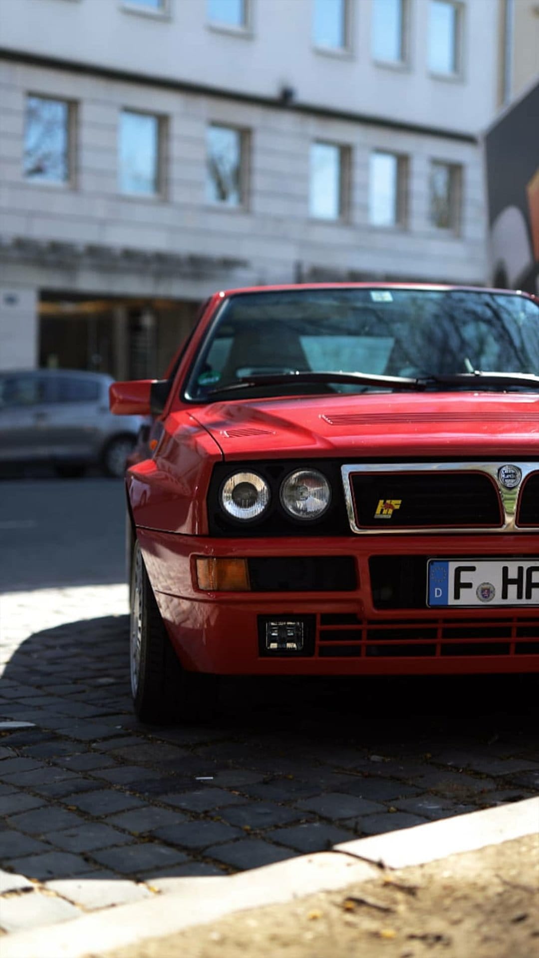 Lancia Delta Integrale Evolution 1 in red parked on a cobblestone street with quad headlights and a front grille.