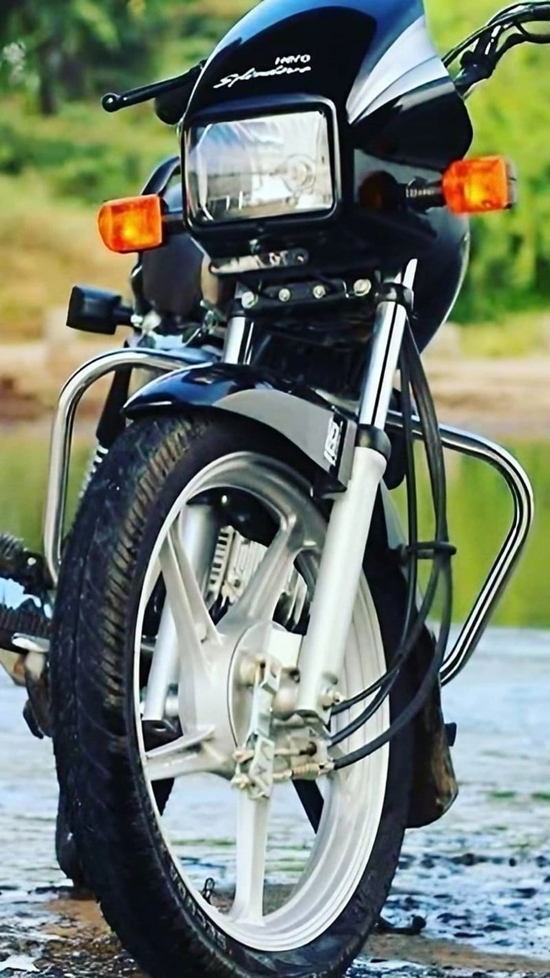 Hero Splendor motorcycle frontal view showing the round headlamp, chrome crash guards, and black alloy wheel.