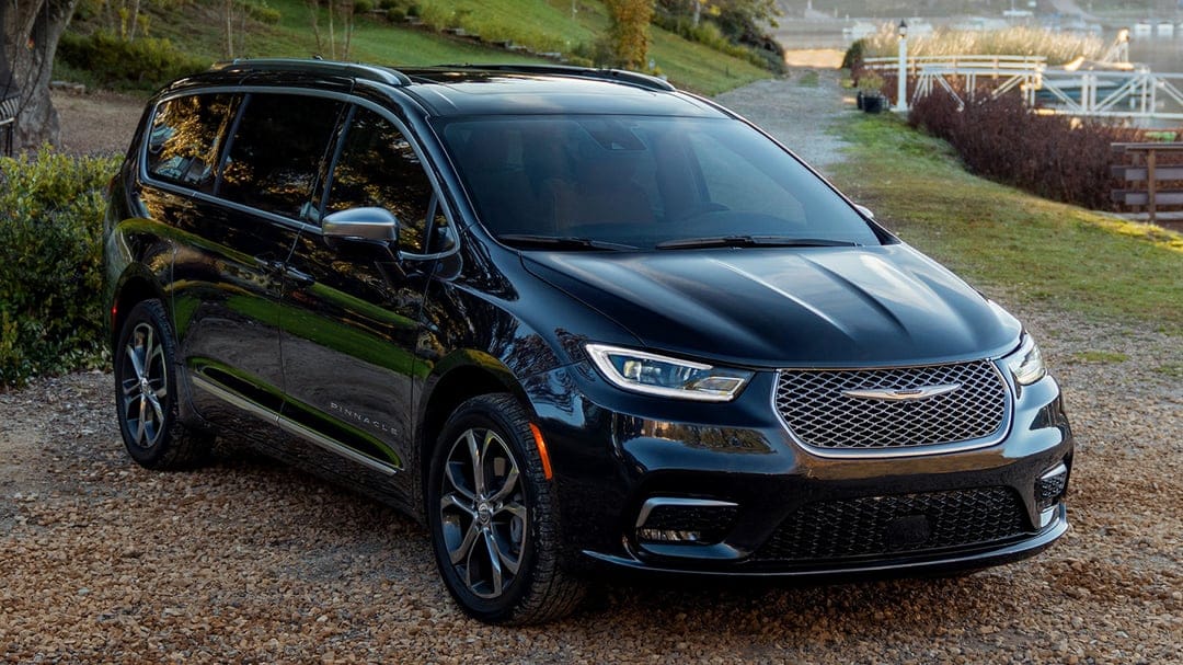 Black Chrysler Pacifica Pinnacle parked on gravel near a lake with warm golden hour reflections and chrome trim.
