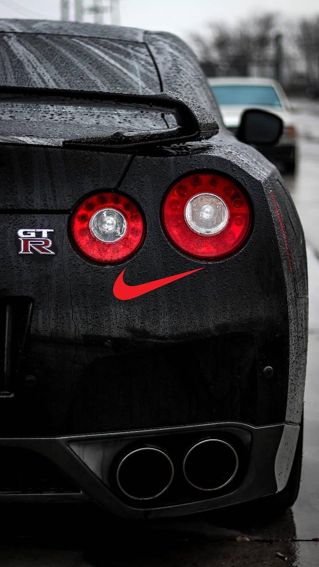 Nissan GT-R taillight assembly with glistening raindrops and a red Nike logo on wet black automotive paint.