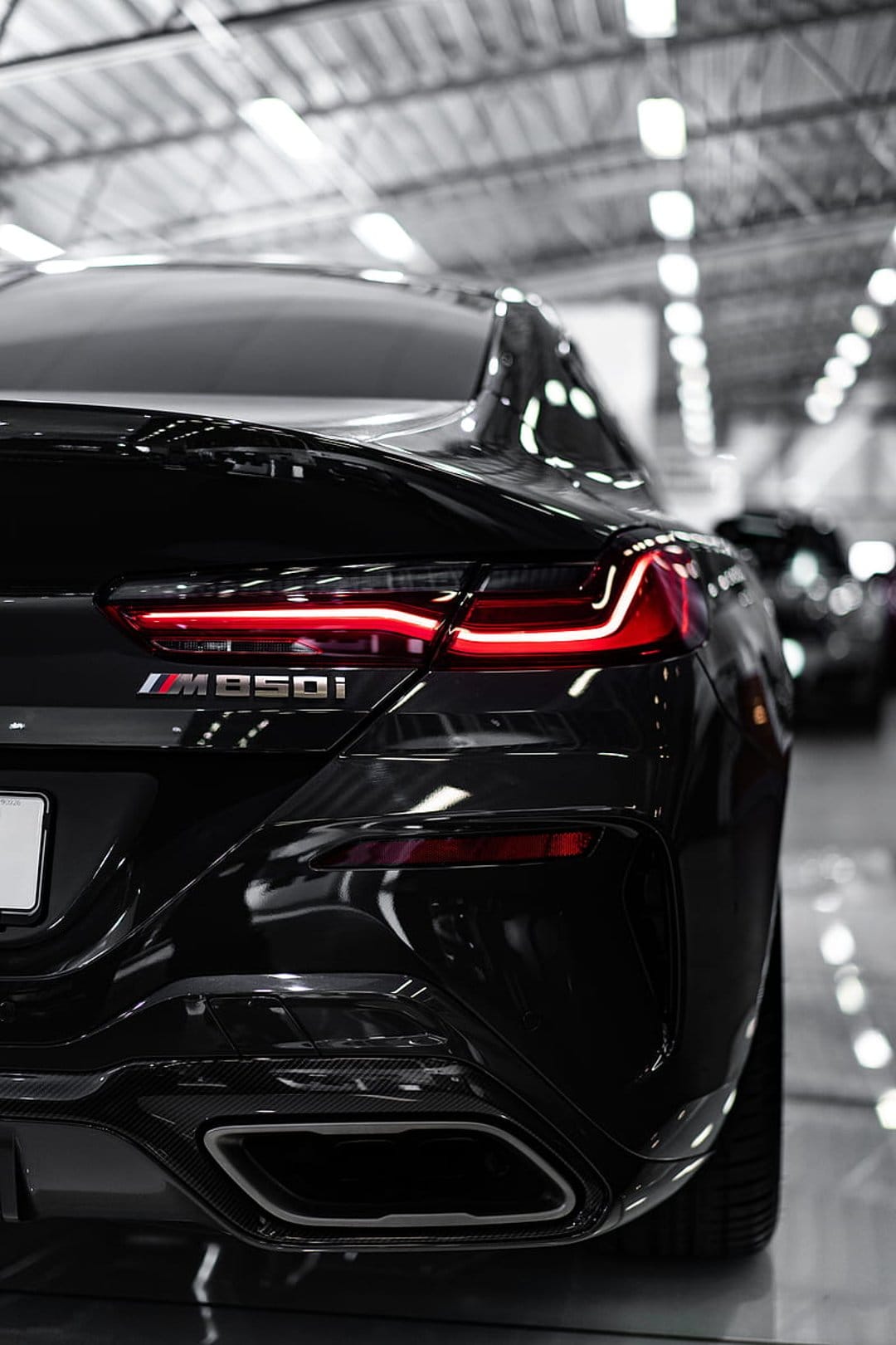 BMW M850i Gran Coupe rear view featuring red LED taillights, carbon fiber diffuser, and quad exhaust pipes.