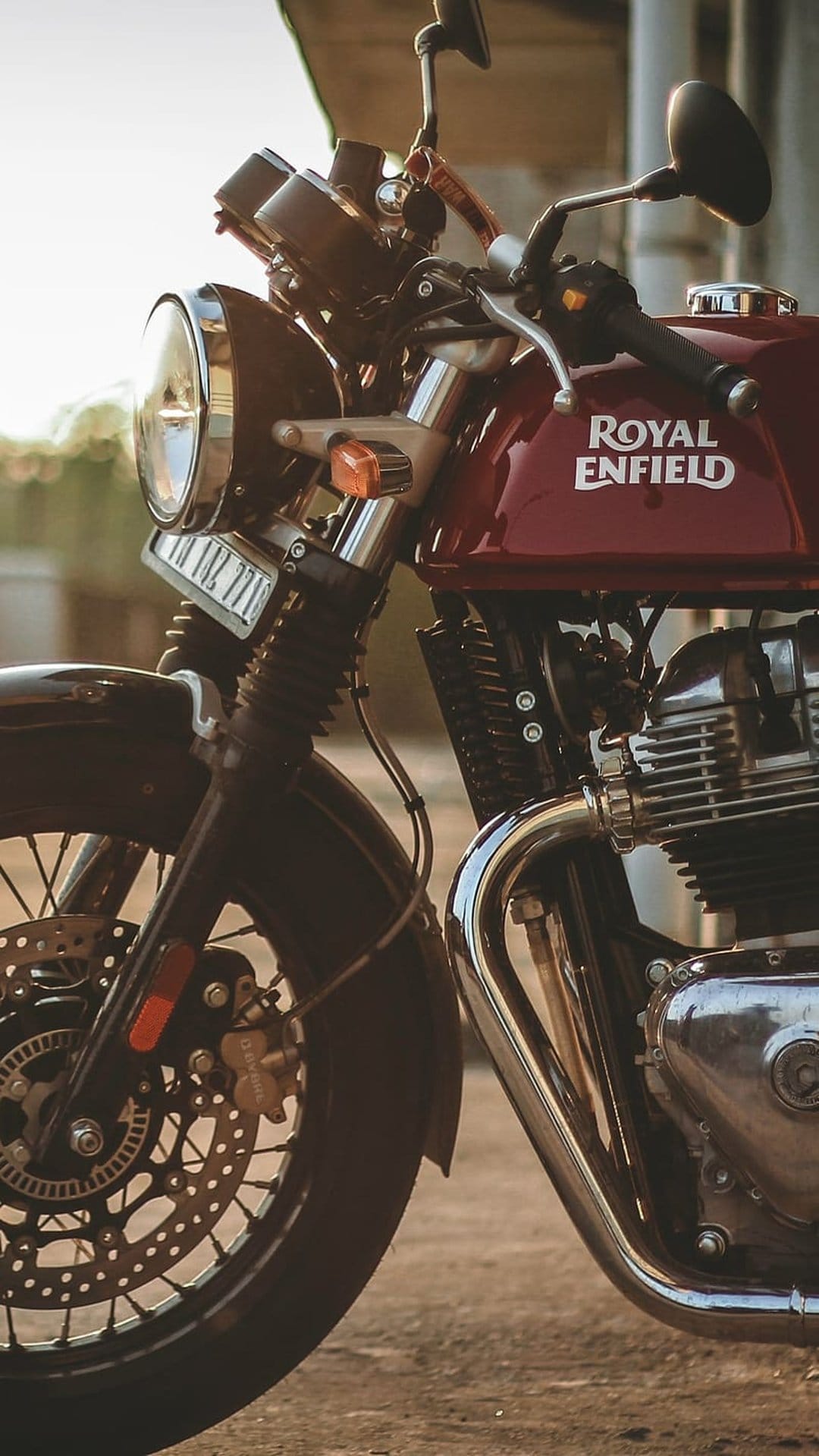 Maroon Royal Enfield motorcycle with chrome details and a front disc brake reflects warm sunset sunlight.