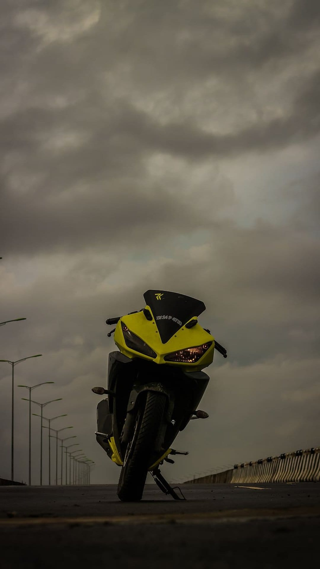 Yellow sports motorcycle with aggressive fairings parked on an asphalt road under a dark overcast sky at dusk.