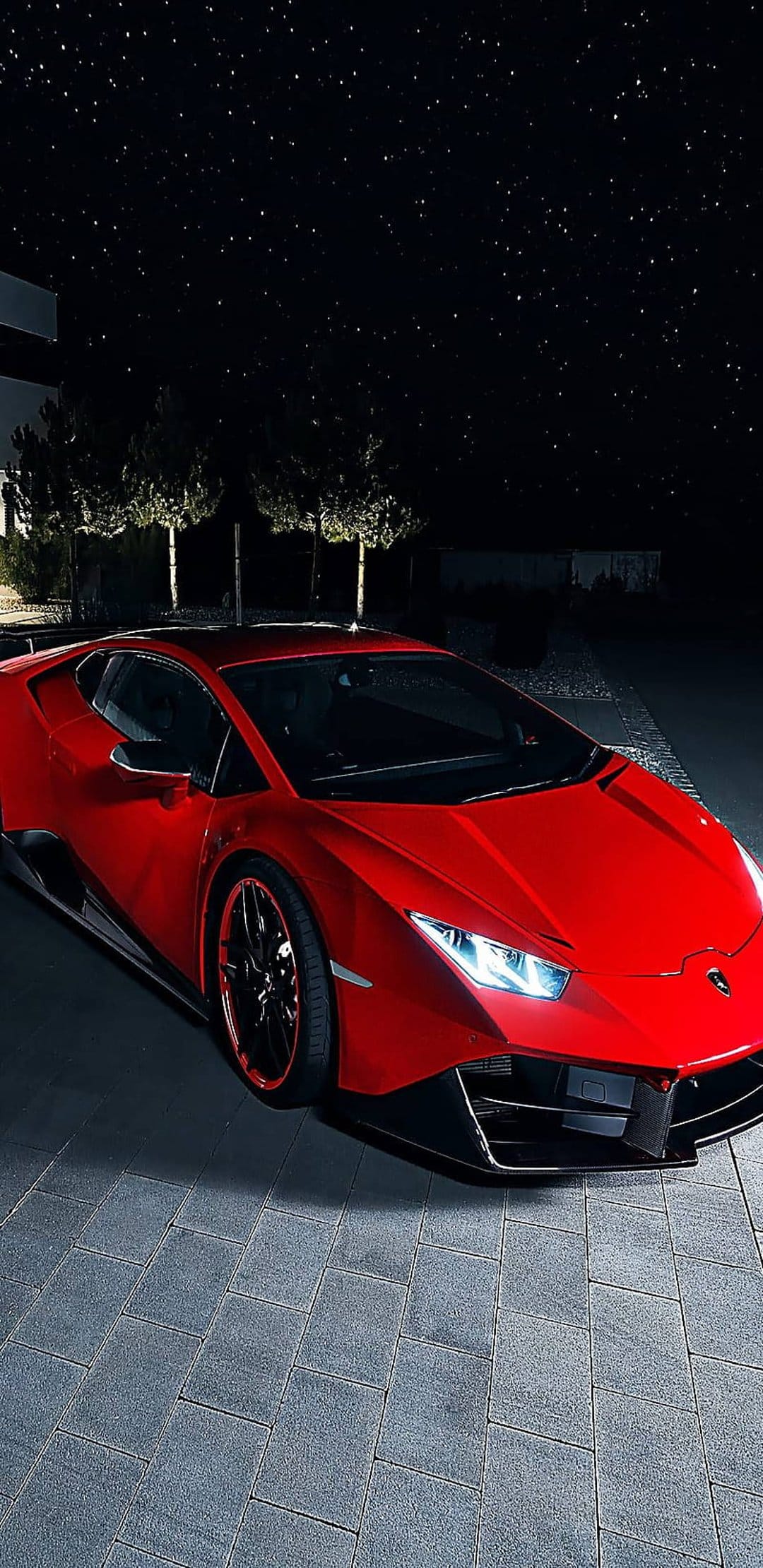 Red Lamborghini with glowing headlights parked on cobblestones under a clear night sky full of bright stars.