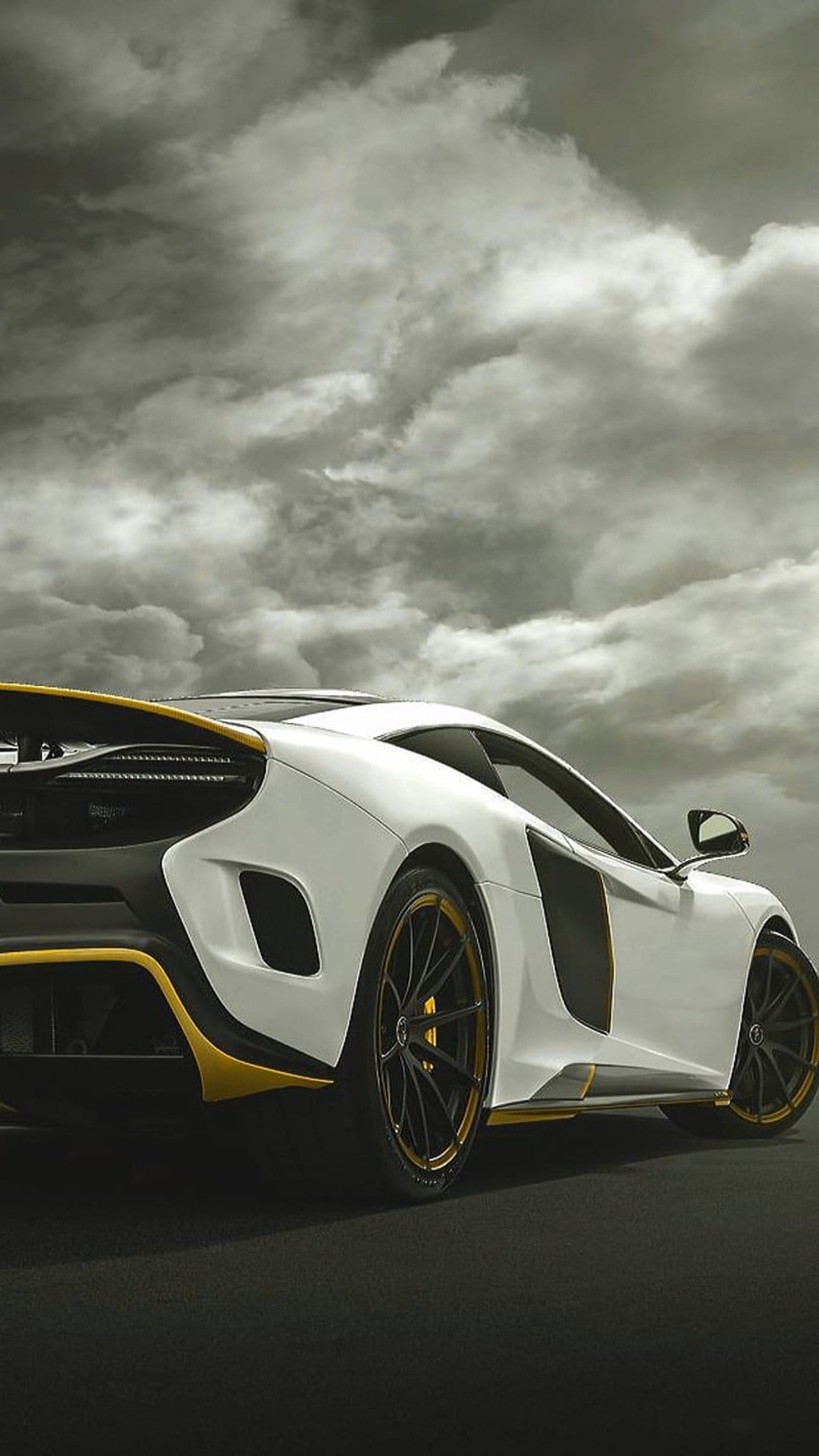 White McLaren supercar with yellow accents parked on a dark road under a dramatic grey sky with turbulent clouds.