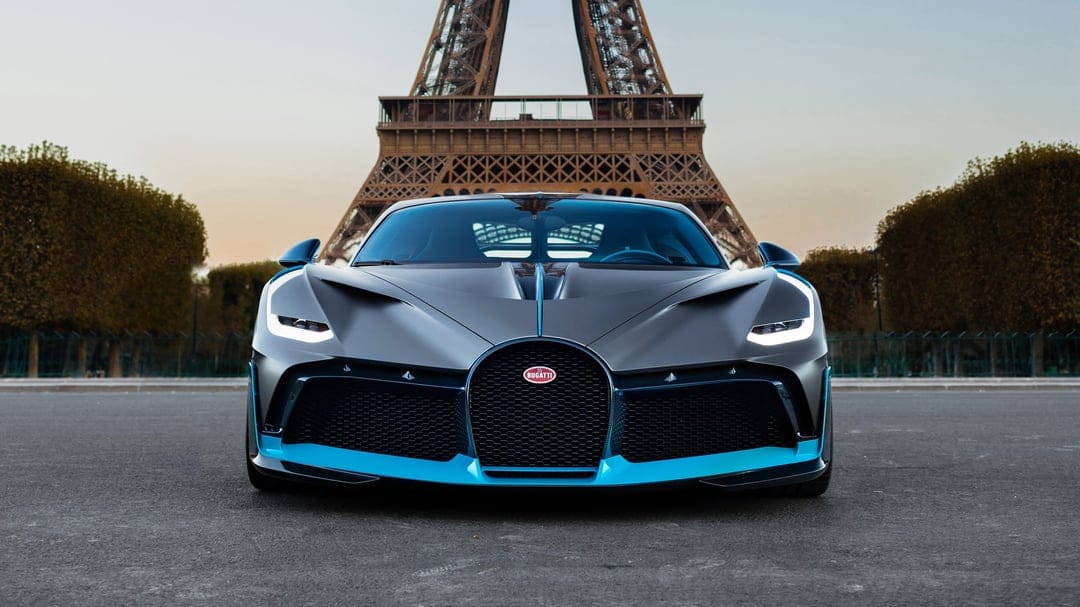 Bugatti Divo hypercar in matte grey and blue parked symmetrically in front of the Eiffel Tower in Paris.