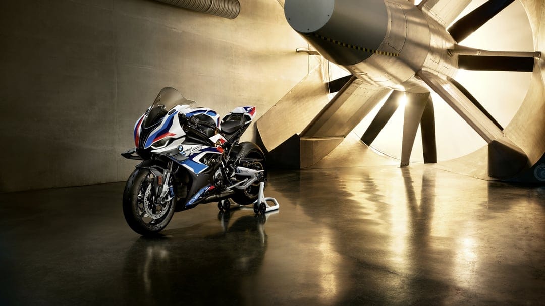 BMW M 1000 RR superbike in a wind tunnel with a massive glowing turbine fan and polished floor reflections.