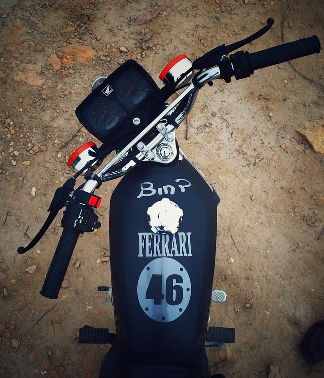 Customized black motorcycle fuel tank with Ferrari decals and racing number 46 viewed from a top-down angle.
