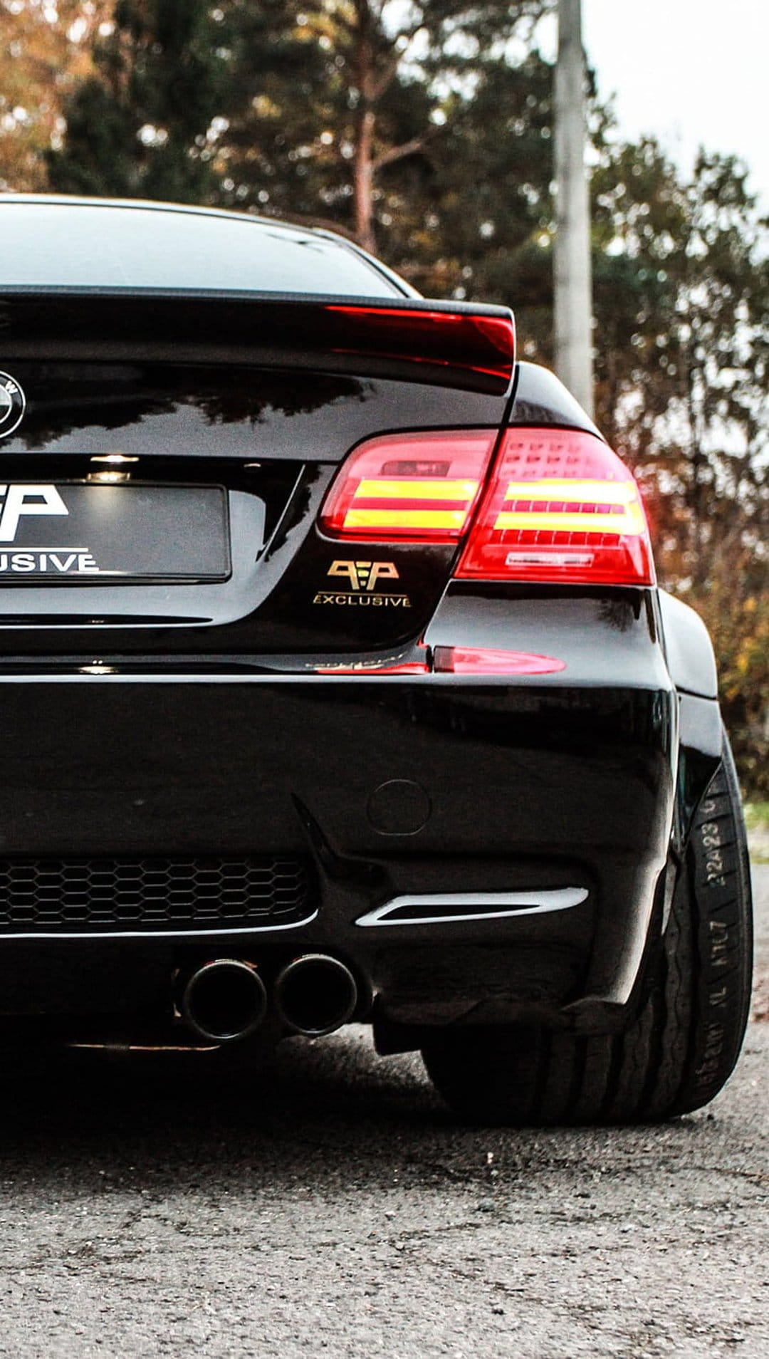 BMW M3 rear view featuring black paint, dual exhausts, a spoiler, and glowing red LED taillights outdoors.