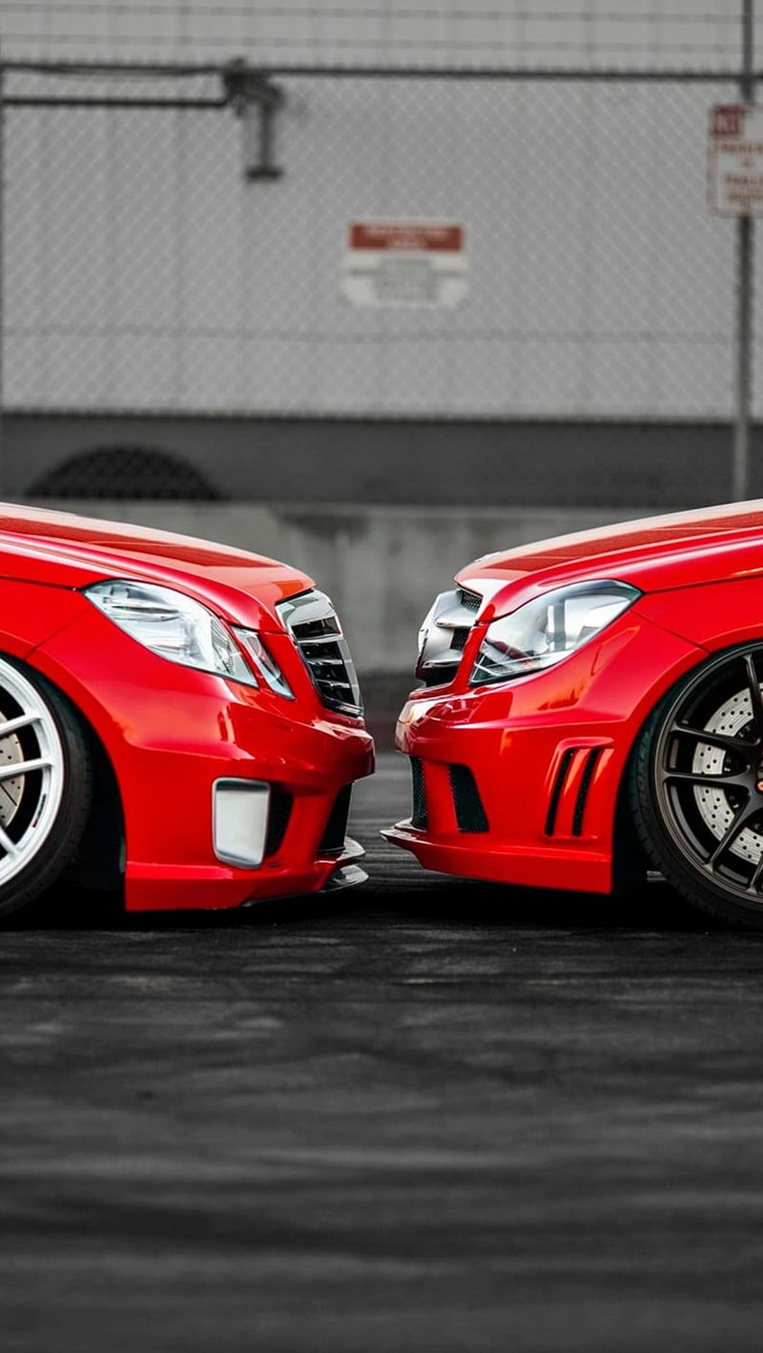 Two red Mercedes-Benz cars with large grilles and LED headlights parked on asphalt in an industrial area.