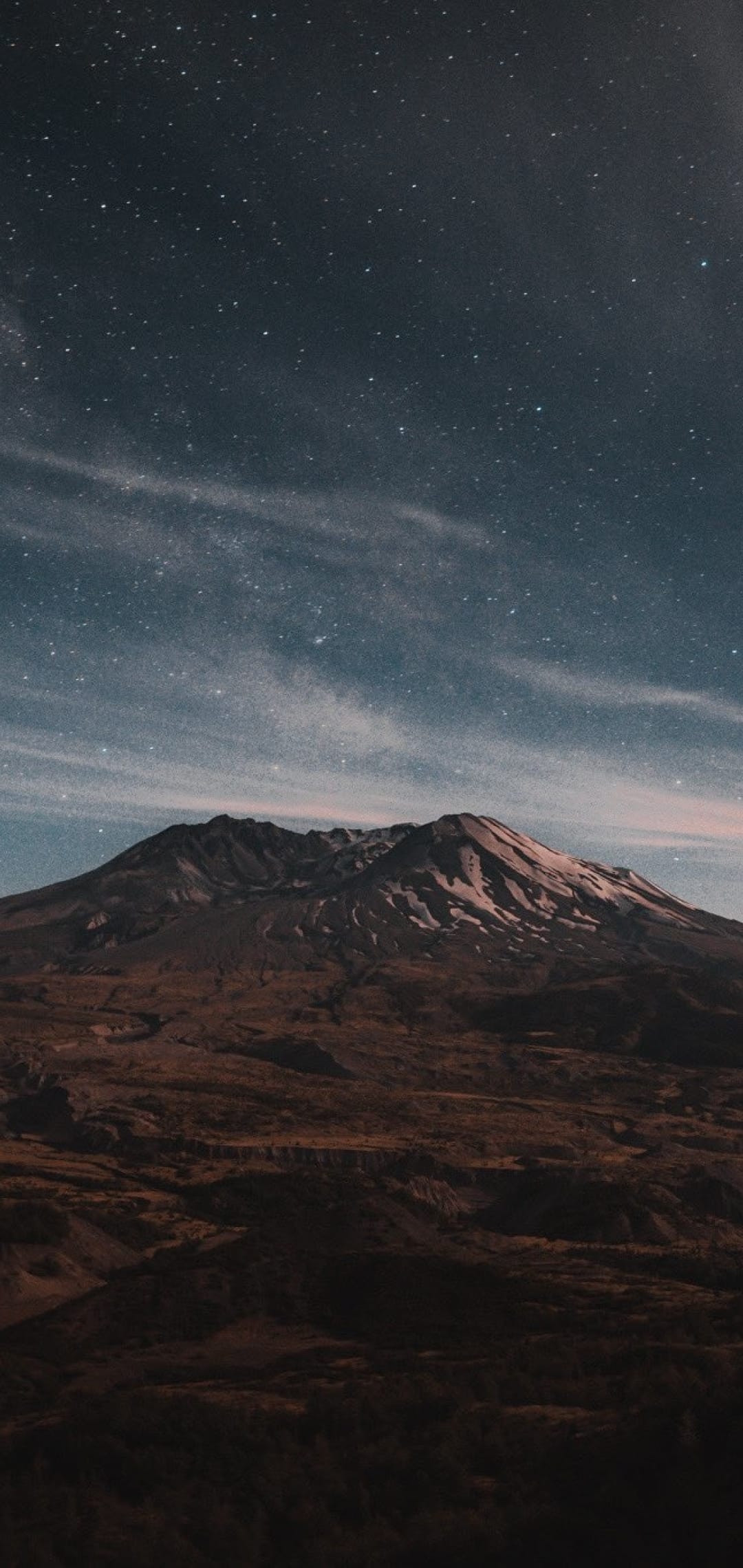 Jagged mountain peak silhouetted against a dense field of glowing stars and wispy cosmic stardust in a dark sky.