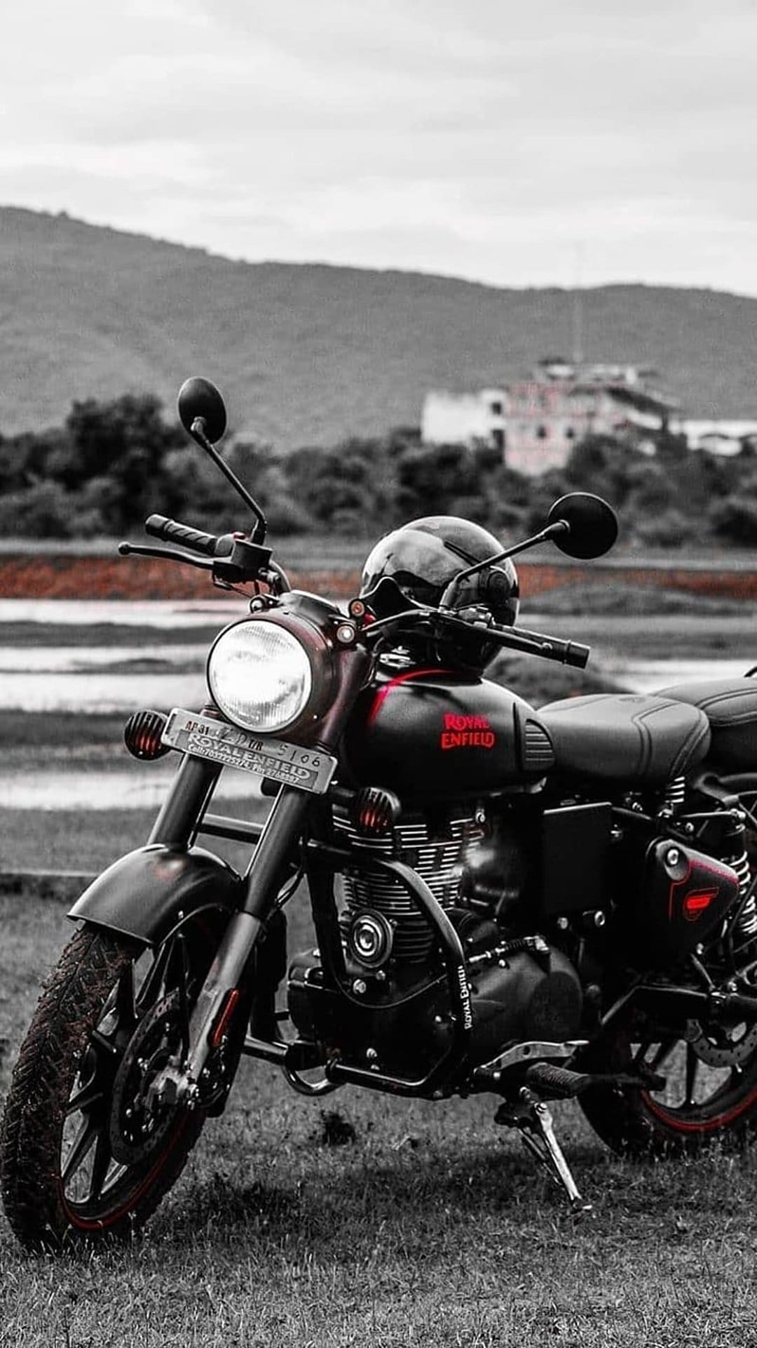 Royal Enfield motorcycle with a black helmet on the handlebars parked in a vast green field under a cloudy sky.