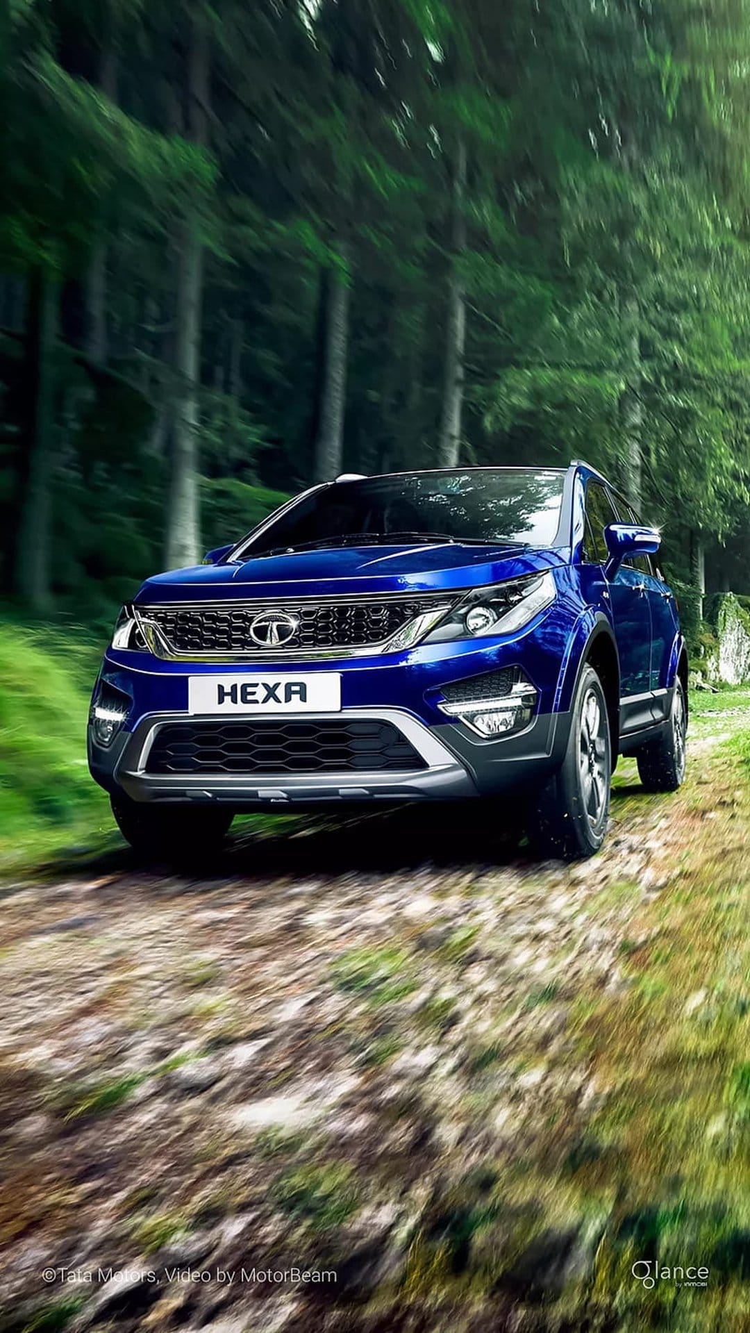 Blue Tata Hexa SUV speeding along a woodland dirt road with visible motion blur and lush greenery.