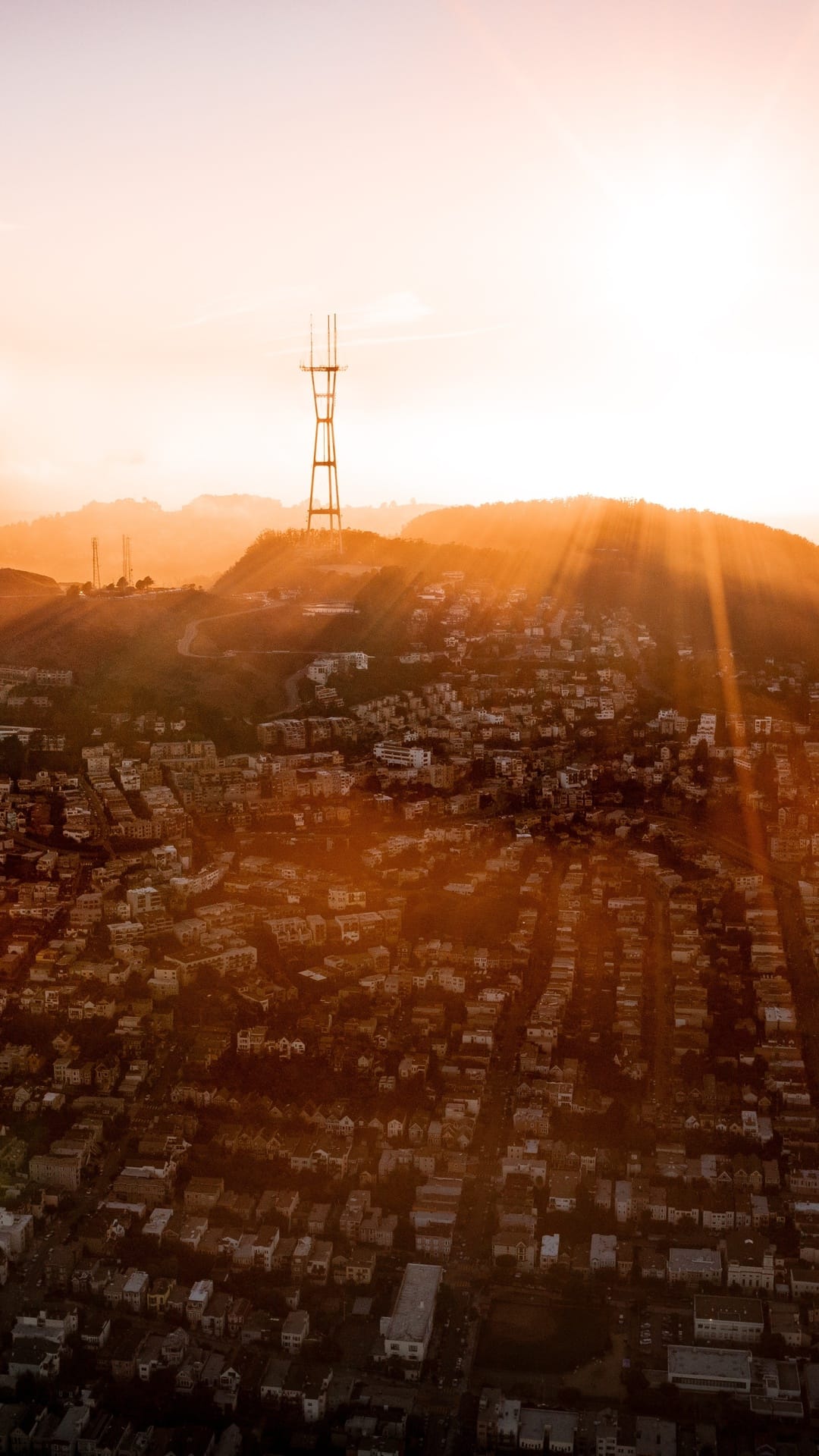Sutro Tower rises above the San Francisco urban sprawl as golden sunset rays illuminate the hazy city skyline.