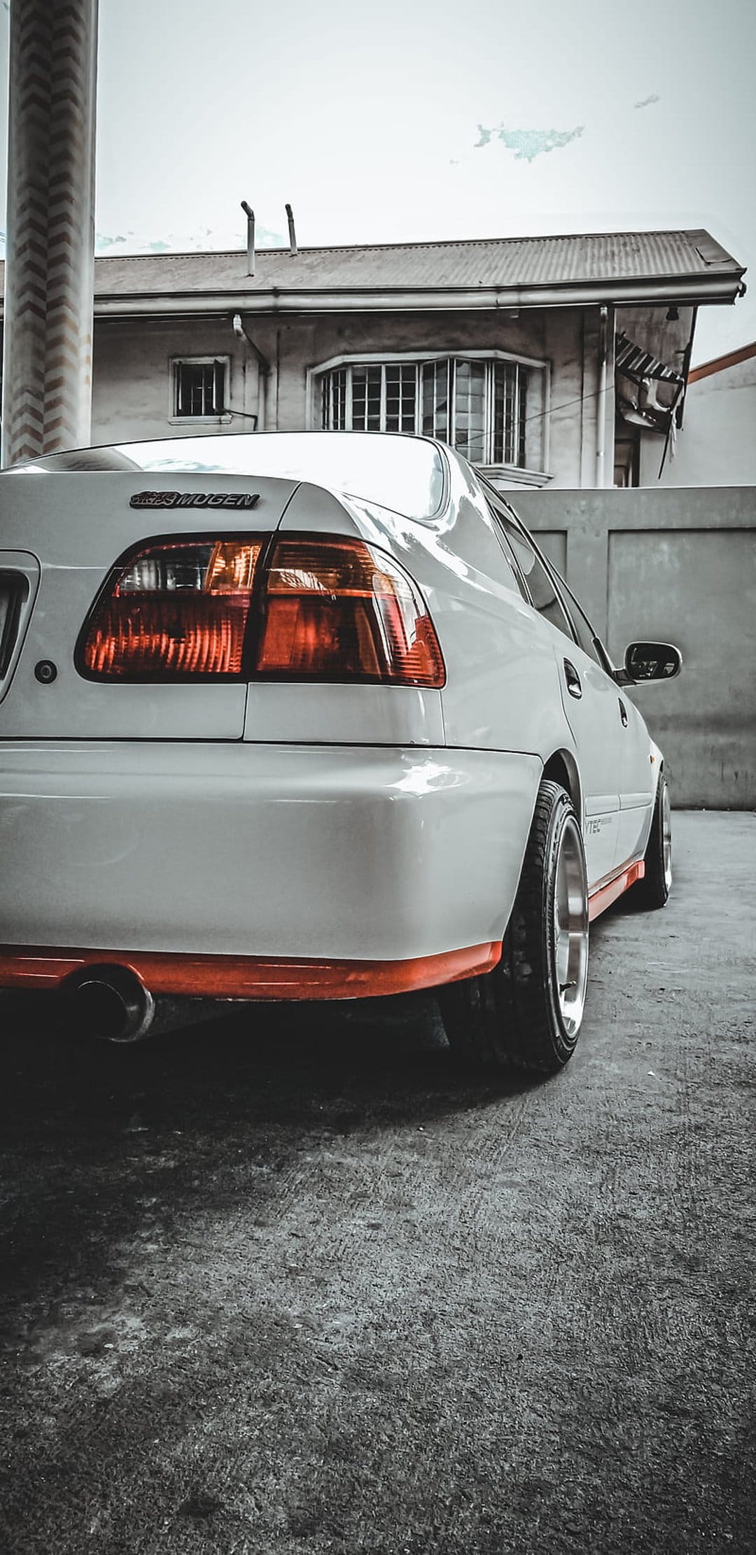 White Honda Civic EG with a Mugen body kit parked on concrete with an orange front lip and exhaust visible.