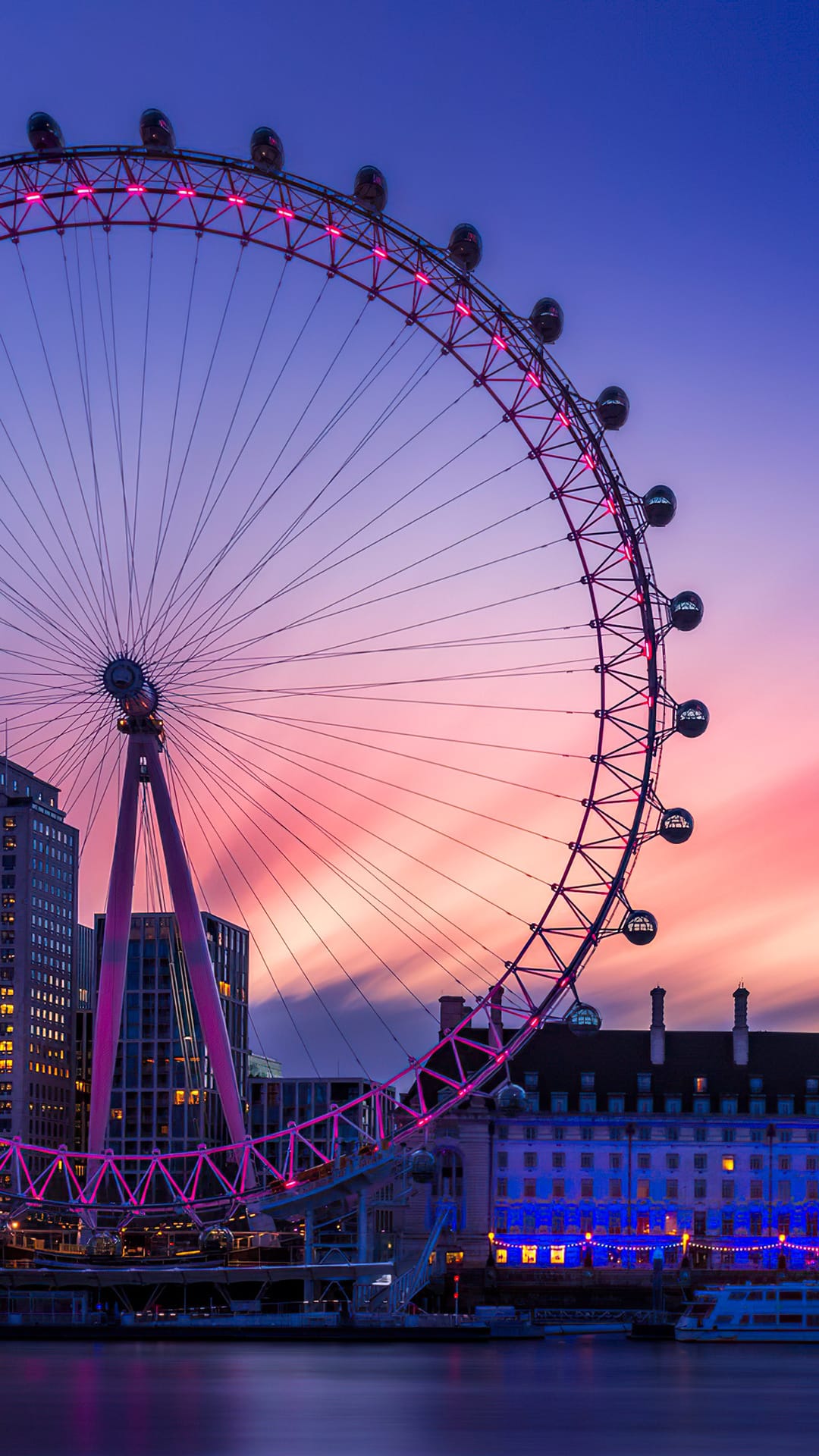 London Eye Ferris wheel silhouetted against a purple and pink sunset sky reflected on the River Thames surface.
