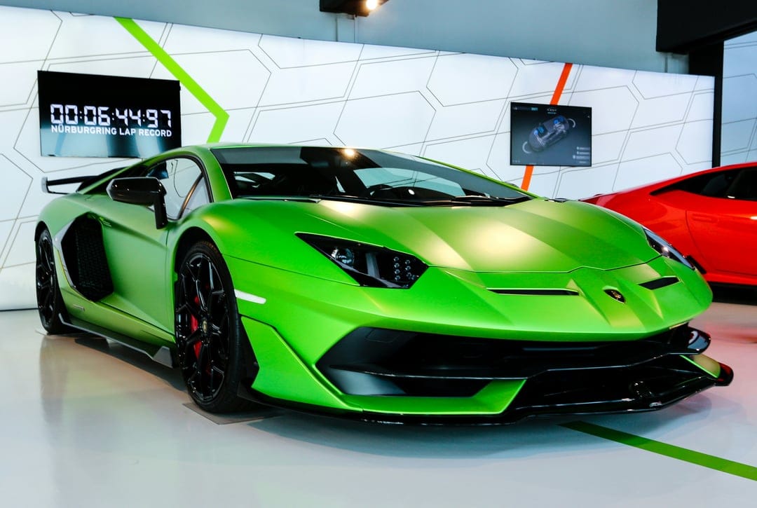 Green Lamborghini Aventador SVJ parked in a showroom next to a digital timer showing a Nürburgring lap record.