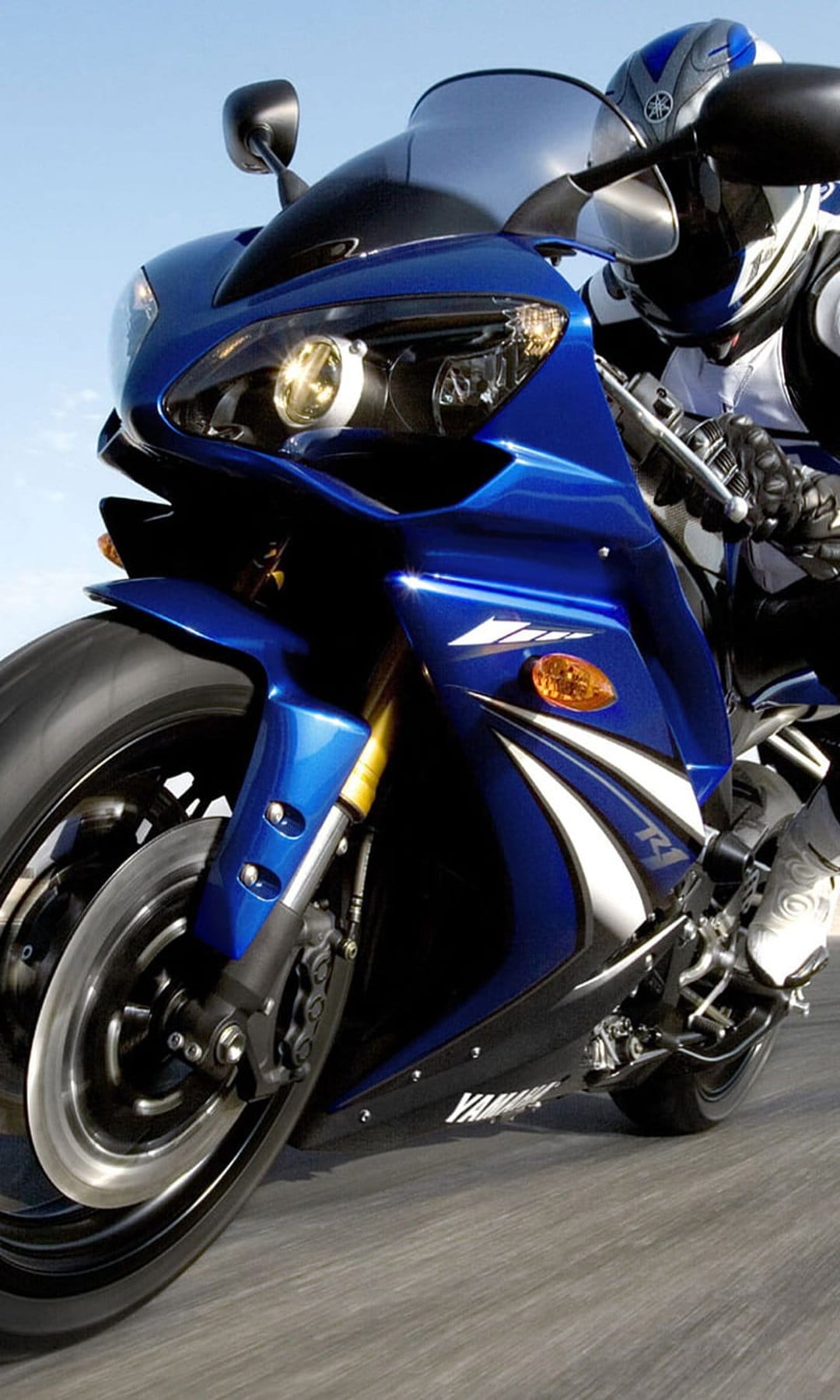 Blue Yamaha R1 motorcycle front fairing and headlights racing on asphalt under a clear sky with motion blur.