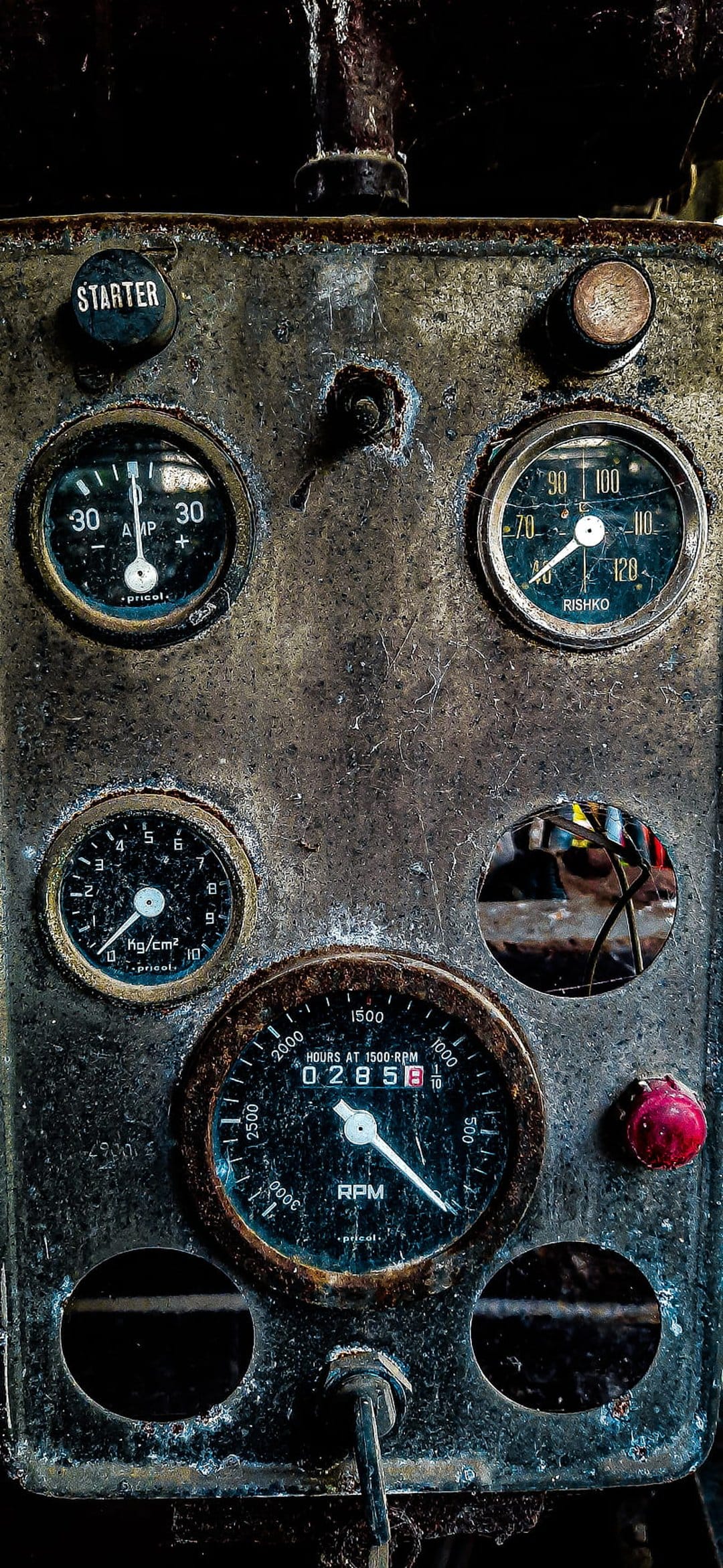 Weathered engine control panel with rusted metal surfaces, analog circular gauges, and a red starter button.
