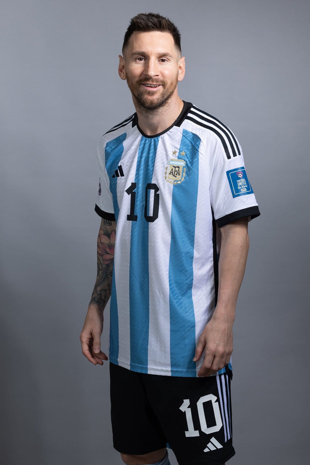 Lionel Messi wearing an Argentina striped jersey and number ten shorts against a solid grey studio background.