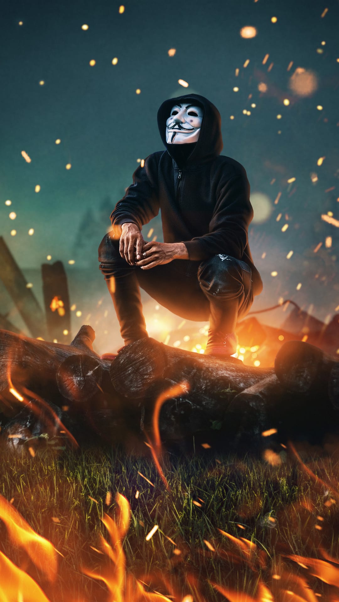Masked figure in a Guy Fawkes disguise crouches on burning timber with bright orange sparks and dark smoke.