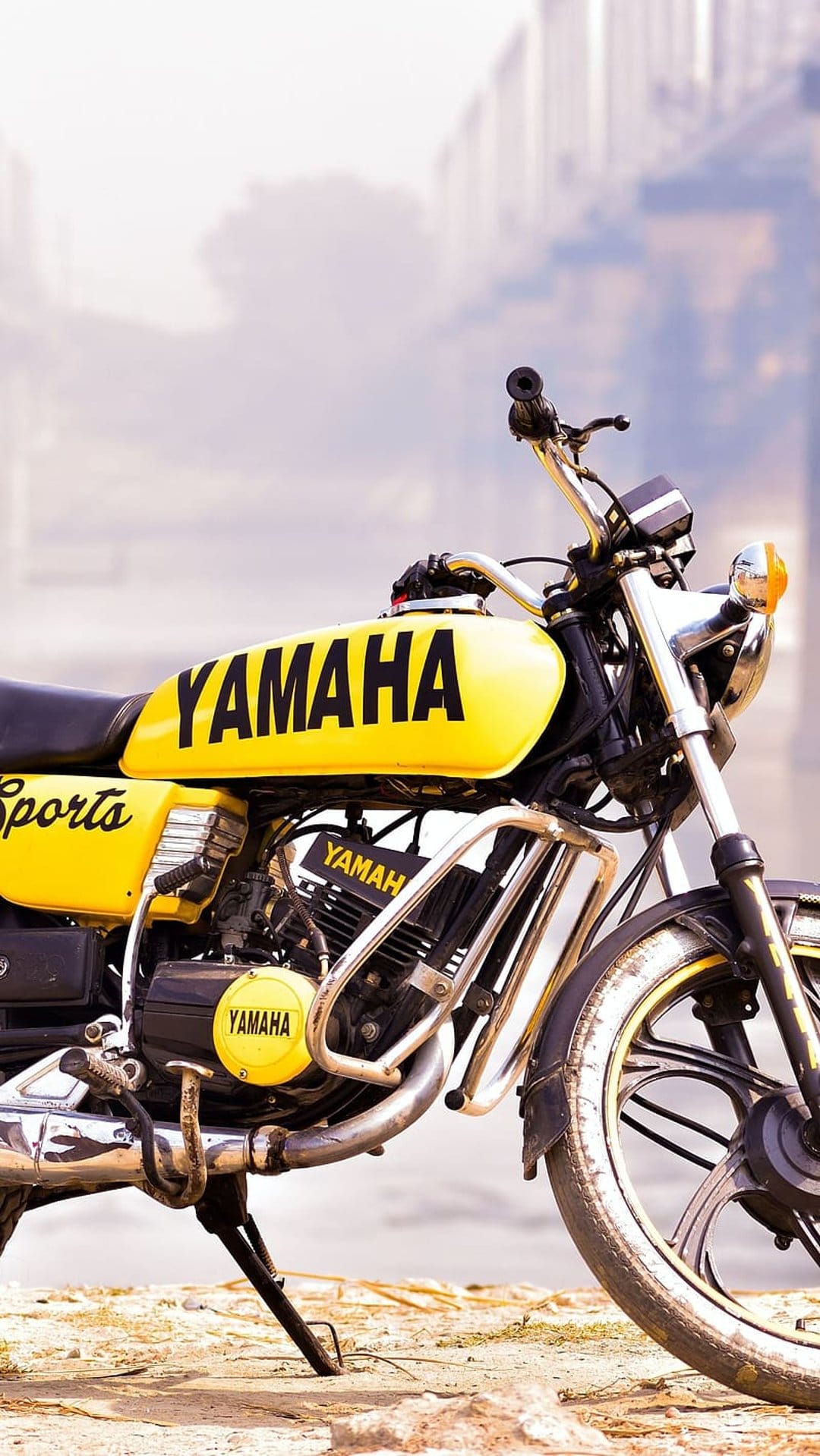 Yellow Yamaha motorcycle fuel tank and engine block shown in a close-up shot with a blurred urban background.